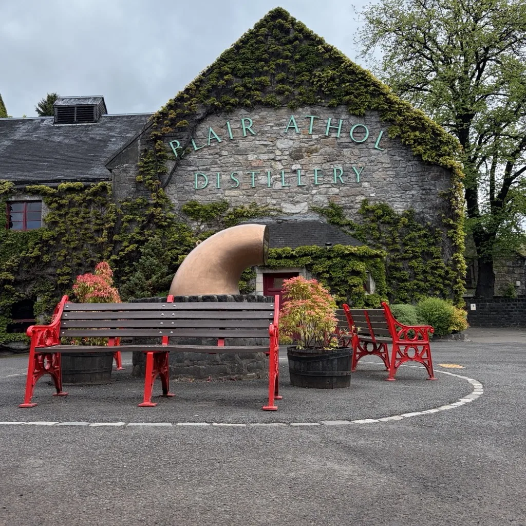 The ivy-clad gable of Blair Athol Distillery with its lettering and red benches in front