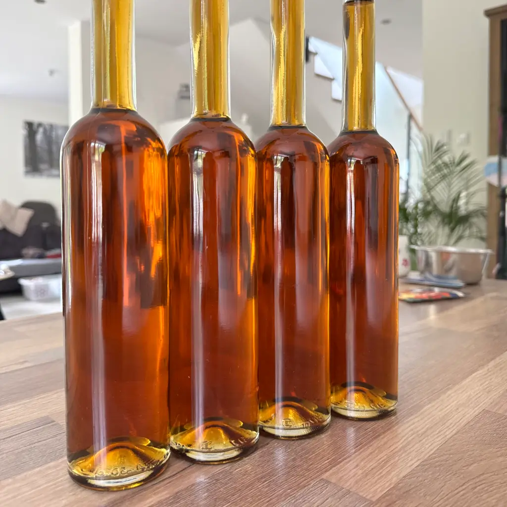 Four bottles of amber, home-matured spirit on a wooden table