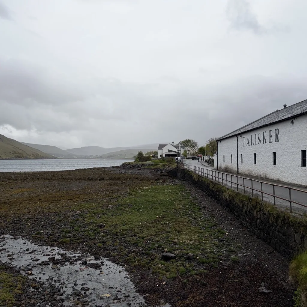 Talisker Distillery on the shore of Loch Harport in grey weather, with the hills of Skye in the background